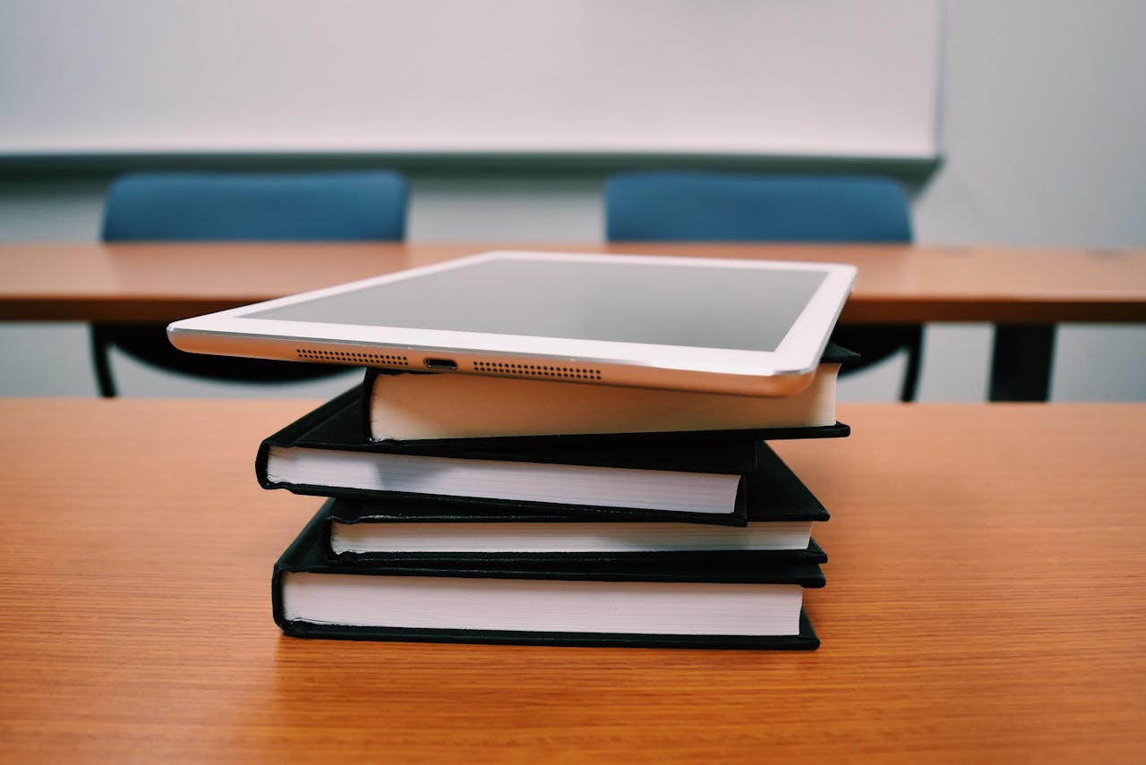 Home A tablet rests on top of a stack of books in an empty classroom, illustrating modern education.